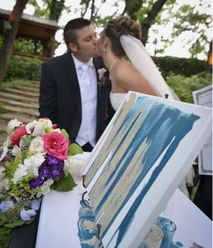 a bride and groom kissing in front of an easel on a table with flowers