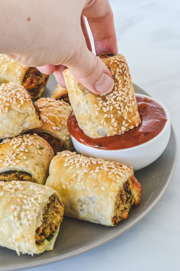 a person dipping sauce on top of pastries in a plate with other food items