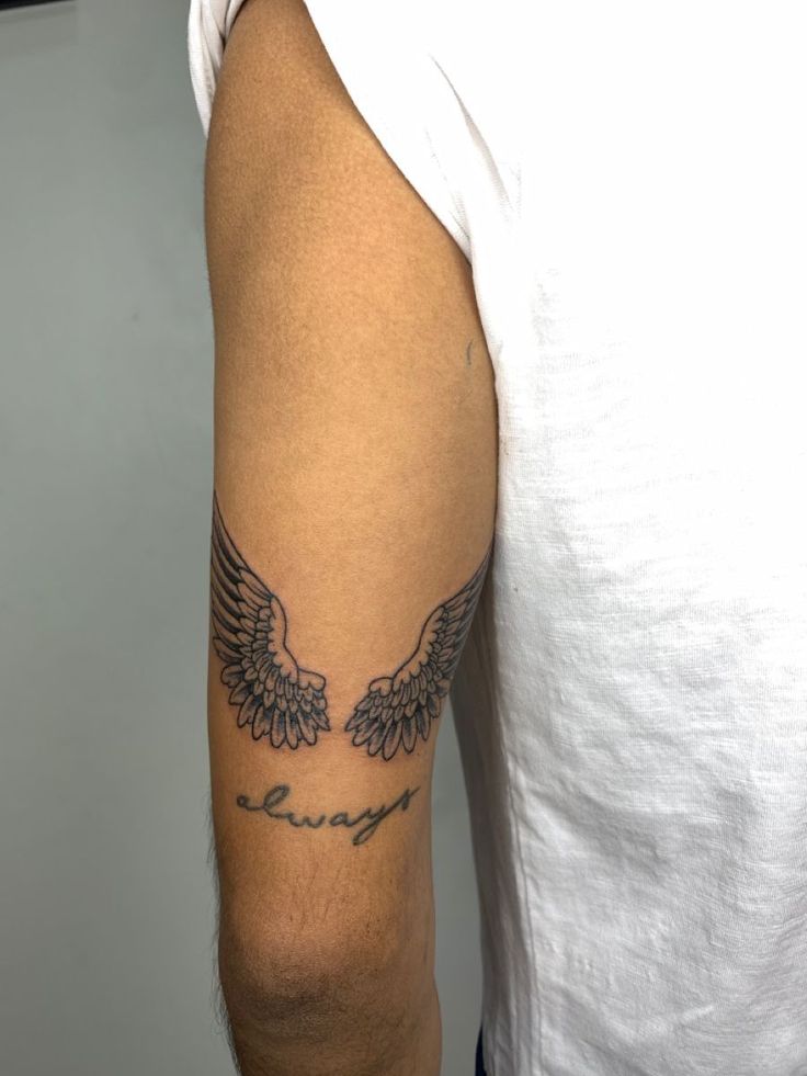 a man with a tattoo on his arm that has two wings and the word love is written in cursive writing