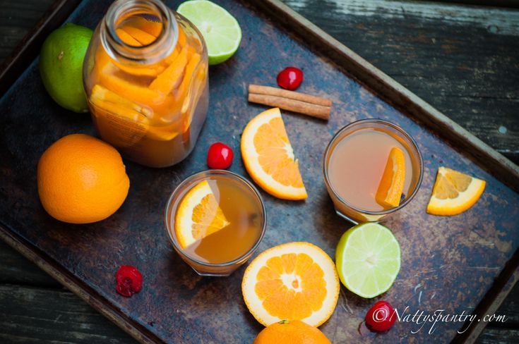 two glasses of orange juice with cinnamon, lime and cherries on a tray next to sliced oranges