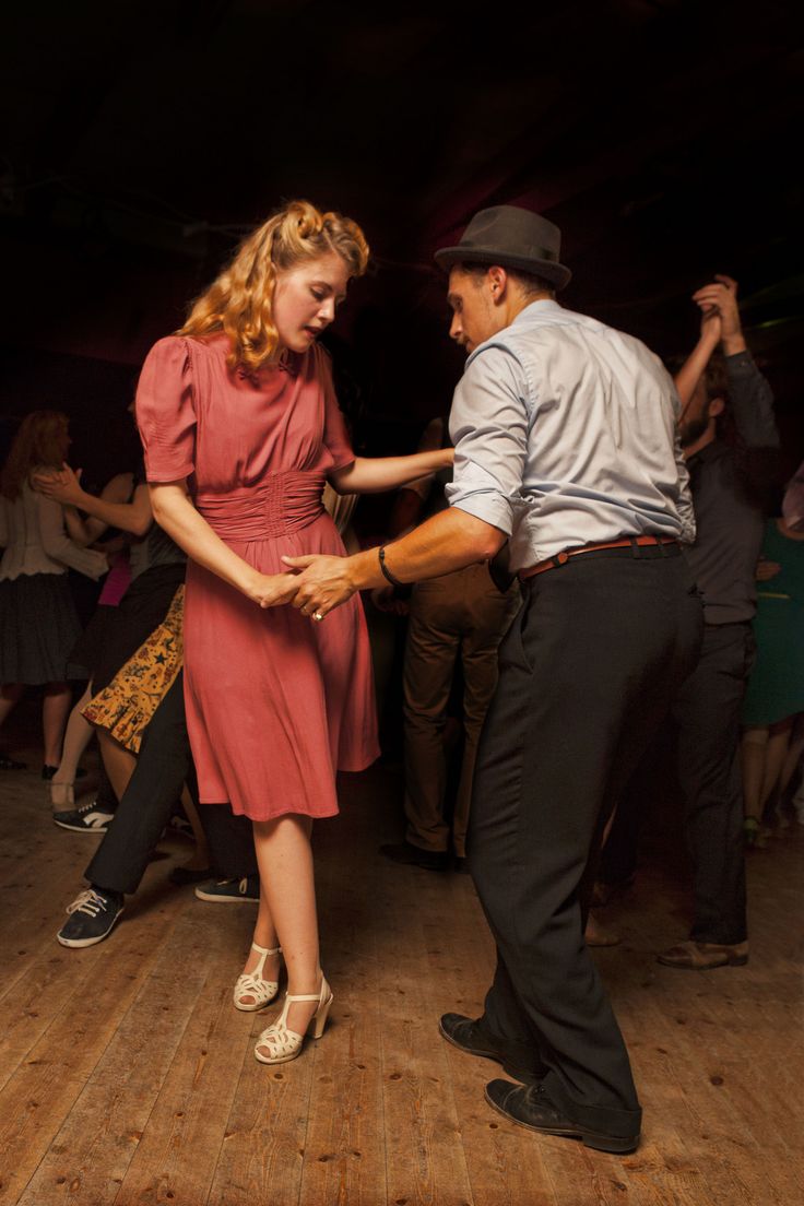 a man and woman dancing on a wooden floor in a dark room with other people