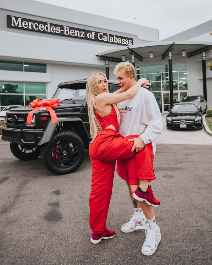 a man and woman standing in front of a mercedes benz dealership with their arms around each other