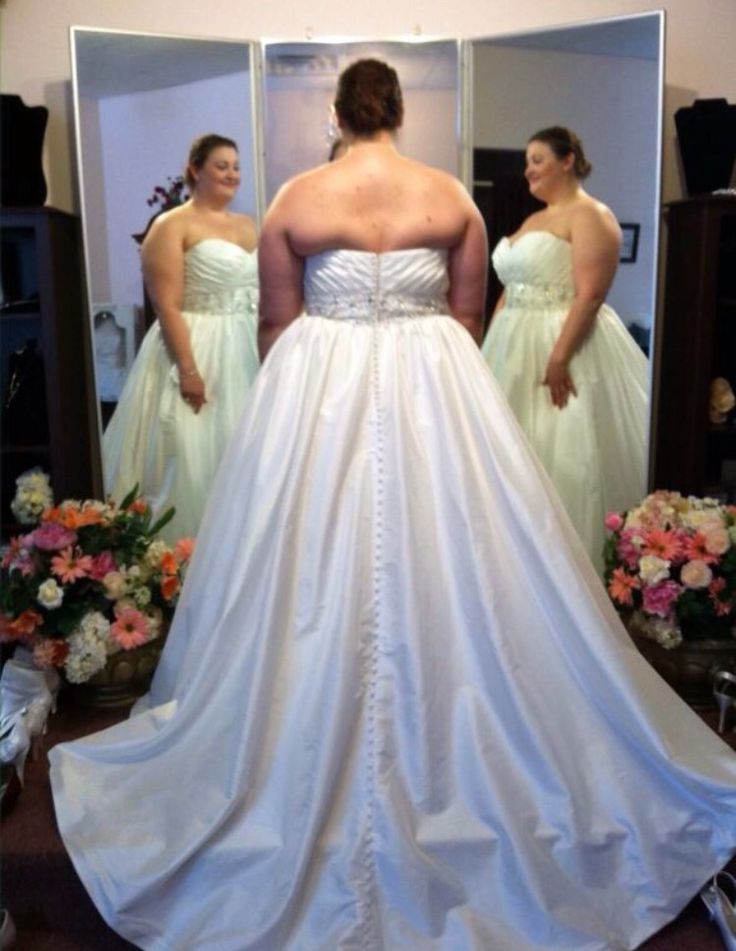 a woman standing in front of a mirror wearing a wedding dress