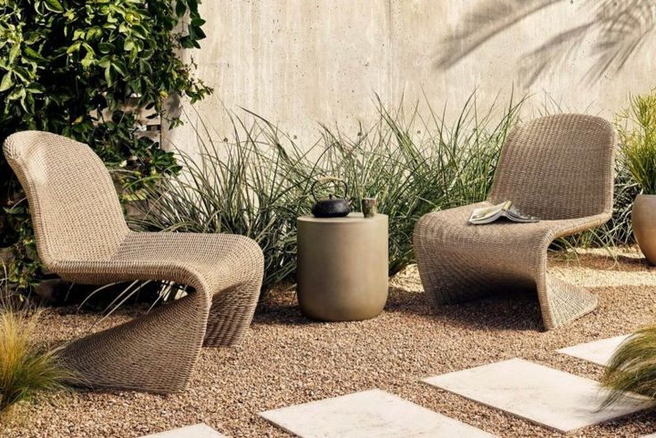 two chairs and a table sitting in the middle of a graveled area next to plants