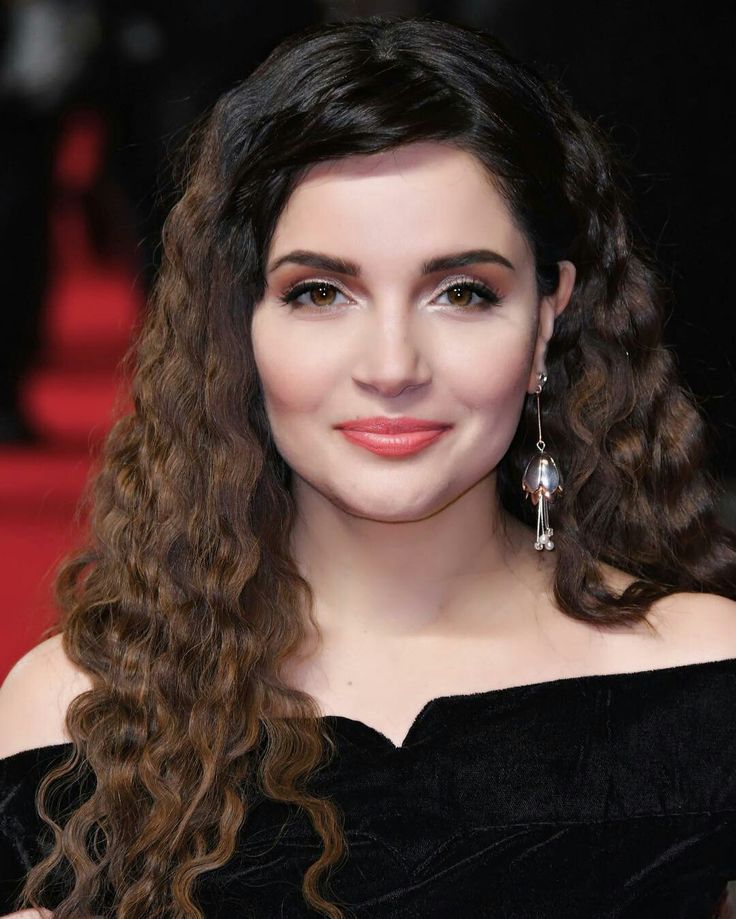 a woman with long curly hair wearing earrings and a black off the shoulder dress is smiling at the camera