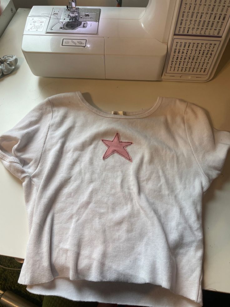 a t - shirt with a pink star on it sitting next to a sewing machine