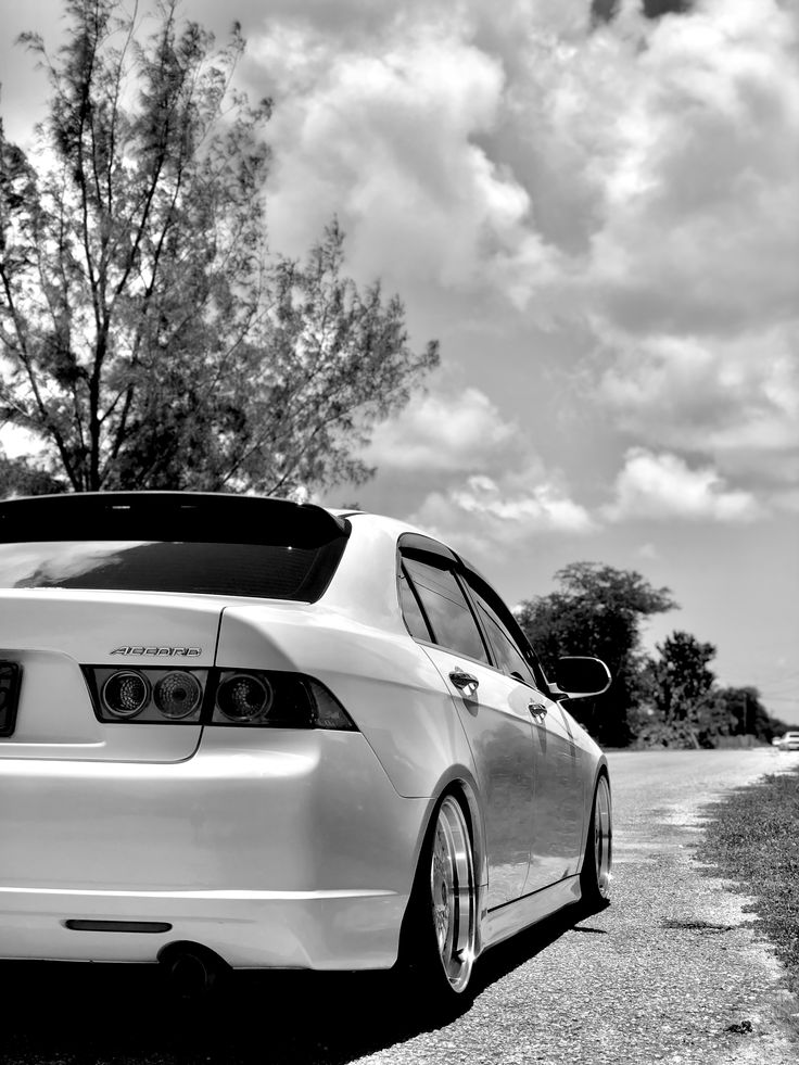 black and white photograph of a car parked on the side of the road with clouds in the background