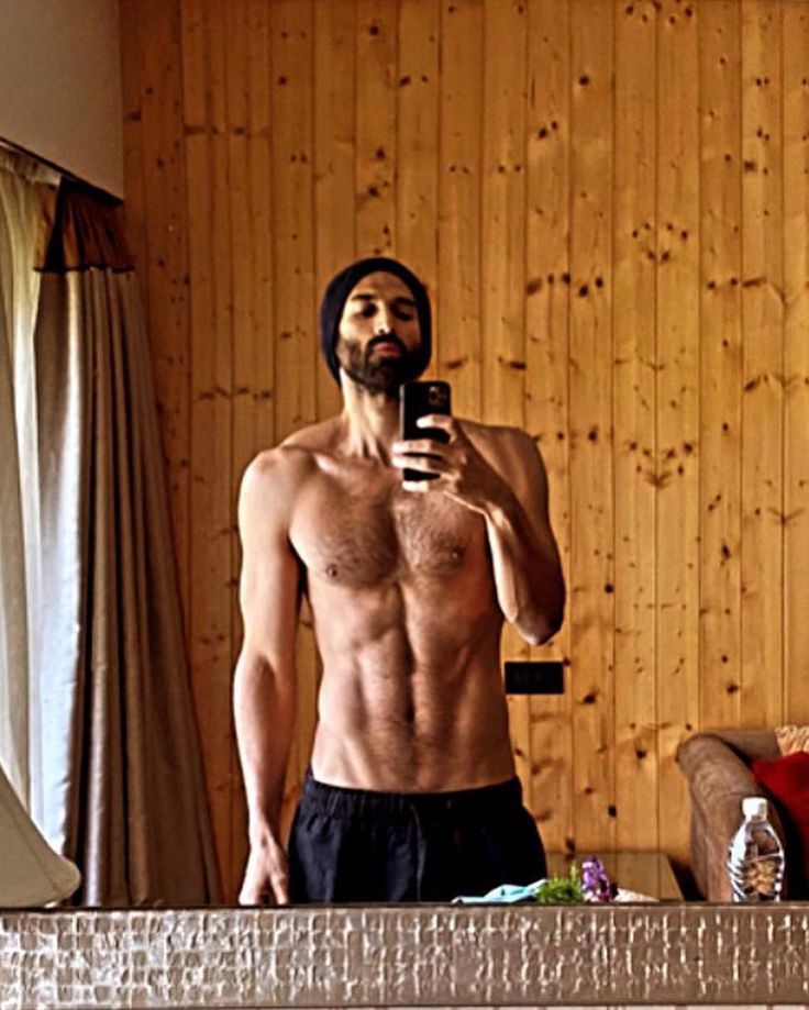 a shirtless man taking a selfie in front of a mirror