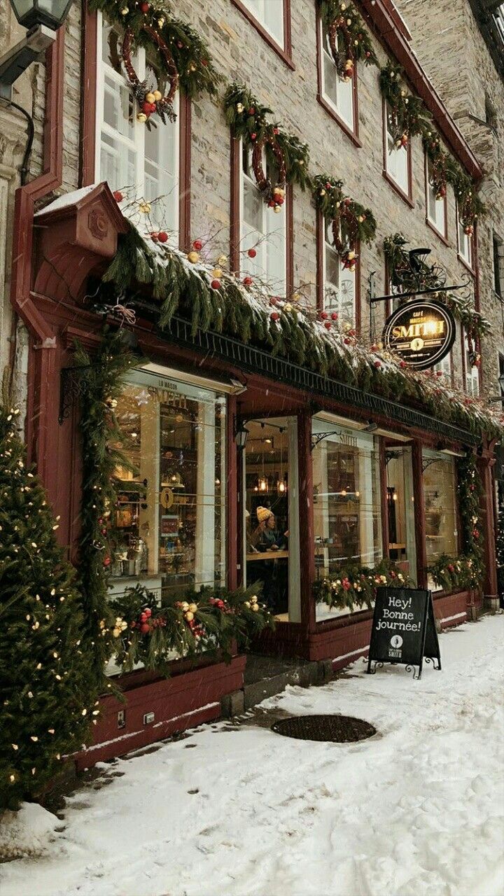 a store front with christmas decorations on the windows and snow covered ground in front of it