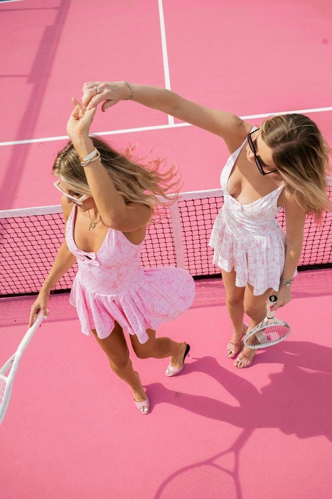 two women in white dresses playing tennis on a pink court with their rackets raised