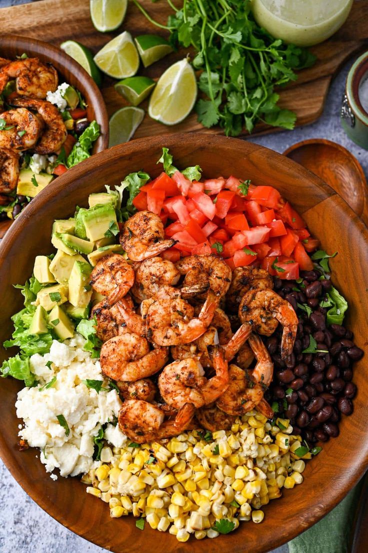 a wooden bowl filled with shrimp salad and black beans, avocado, tomatoes, corn, cilantro, lettuce