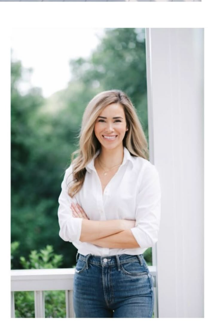 a woman with her arms crossed standing in front of a window and smiling at the camera