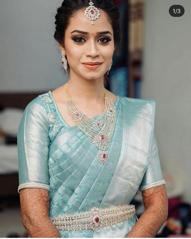 a woman in a blue sari with jewelry on her neck and hands behind her back