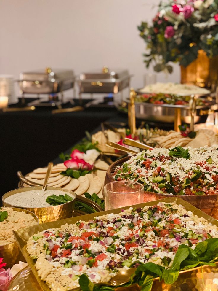 many different types of food are lined up on a buffet table with flowers in the background