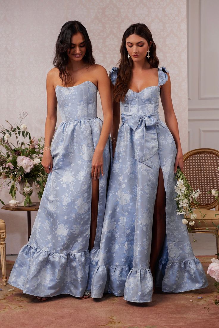 Introducing The Charlotte Dress! She's the perfect strapless gown featuring all things classy and elegant. She's made in our Denim Blue Windsor brocade, which features blue florals on a blue background, and flaunts a flirty side-front slit. Fall in love with beautiful boning details at the bodice, a stunningly laced corset back, and the sweetest gathered bottom ruffle tier for any and all occasions. Gizele is 5’9 and is wearing a size 2. Please note color shade may vary between styles, fabrics o Blue Satin Floral Dress, Bow Back Bridesmaid Dress, Classic Timeless Bridesmaid Dresses, Mis Match Blue Bridesmaid Dresses, Classy Bridesmaids Dresses, Blue Mother Of The Bride Dresses, Light Blue Formal Dresses, French Blue Bridesmaid Dresses, Blue Mother Of The Bride Dress