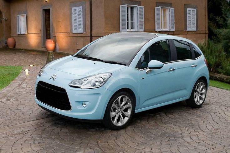 a small blue car parked in front of a house on a cobblestone driveway