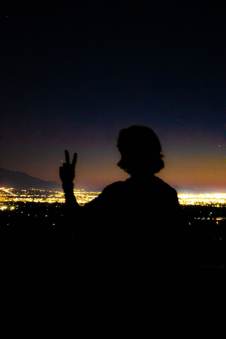 the silhouette of a person with their hand up in the air at night over a cityscape