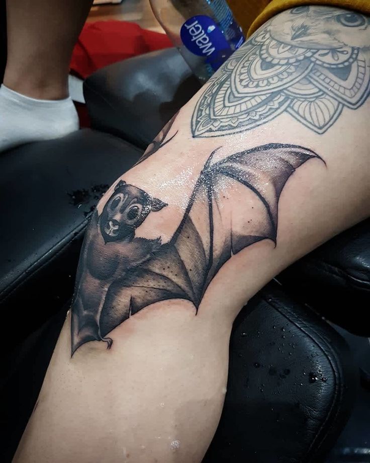 a black and white photo of a bat on someone's leg, with tattoos