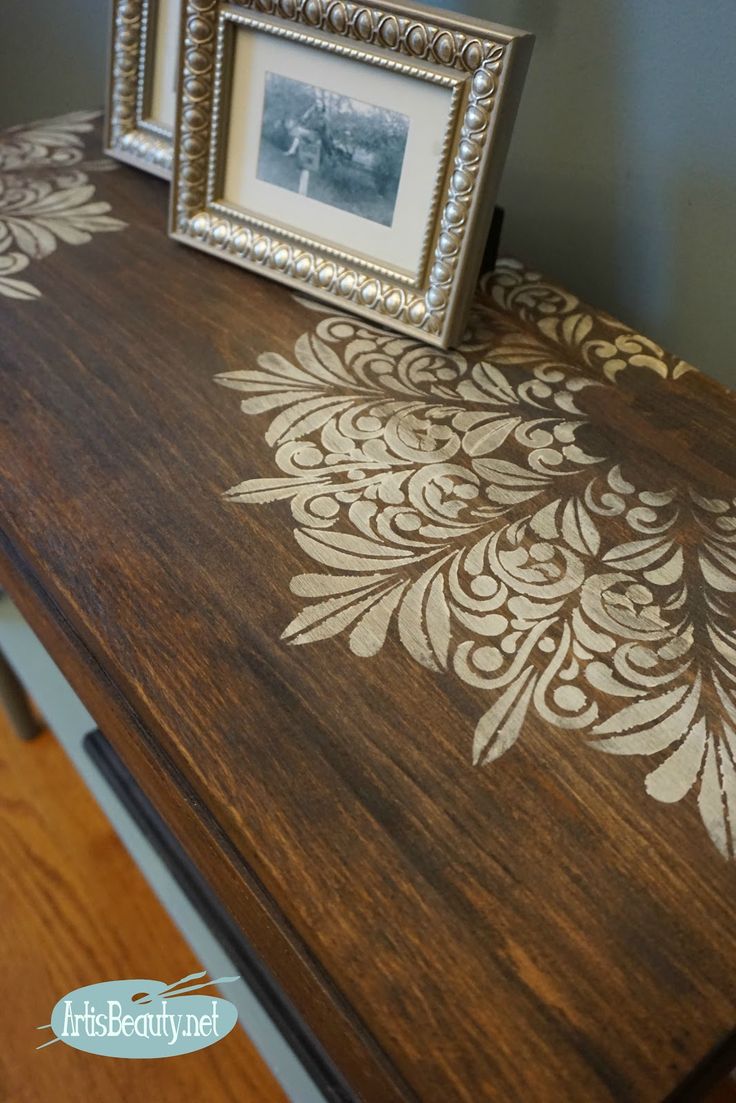 a wooden table with an ornate stencil design on it and two framed photos