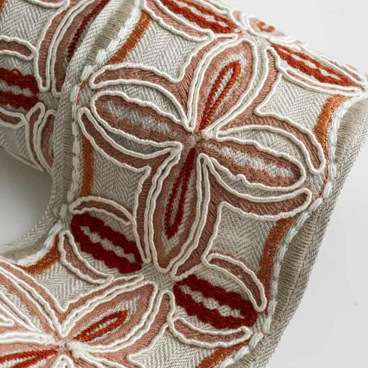 an orange and white pillow with red flowers on it's back side, sitting on a white surface