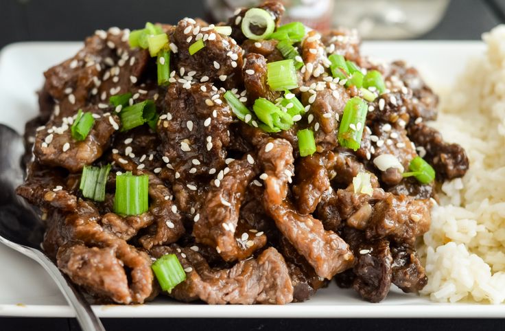 a white plate topped with meat covered in sesame seeds and green onions next to a fork