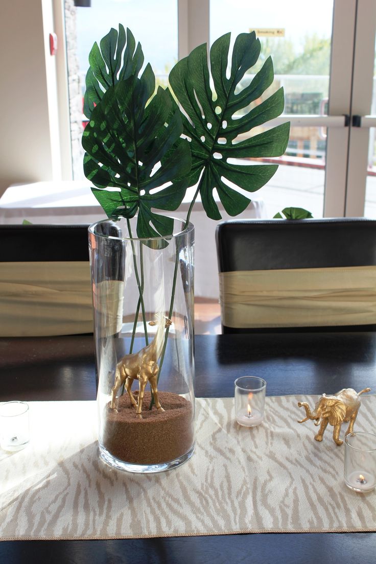 a vase filled with fake plants on top of a wooden table next to a window