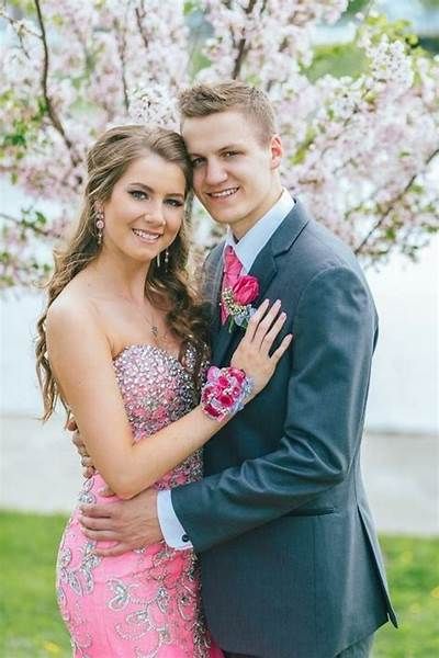 a young man and woman posing for a photo in front of a tree with pink flowers