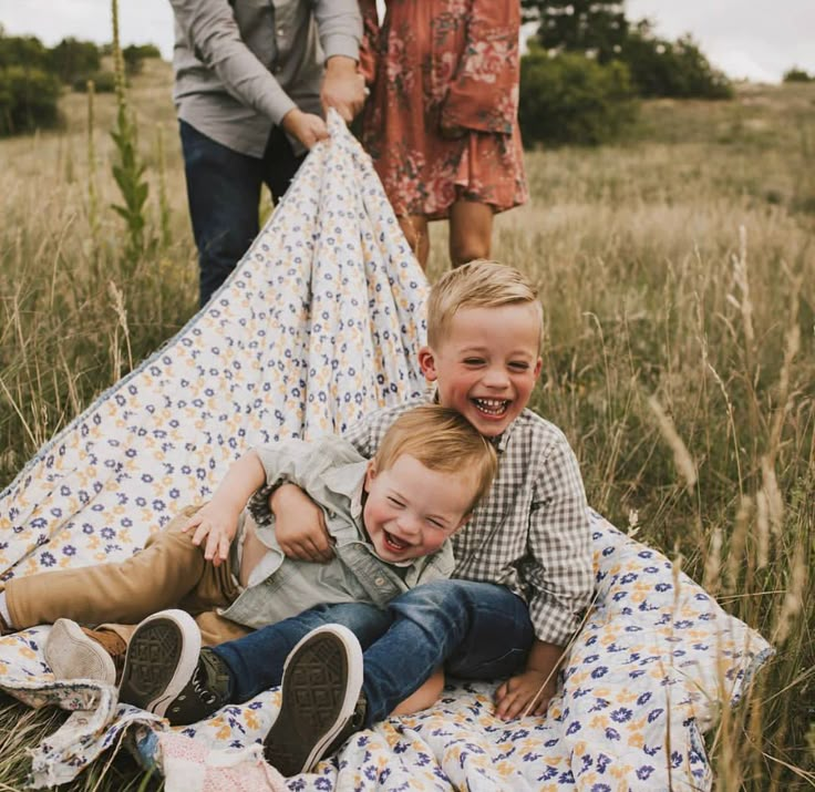 two young boys sitting on top of a blanket in a field next to an adult