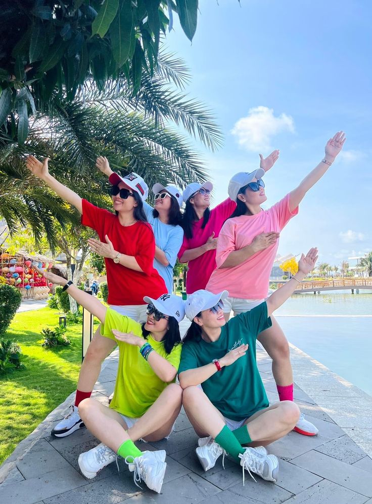 five people posing for a photo in front of a tree and water with their arms up