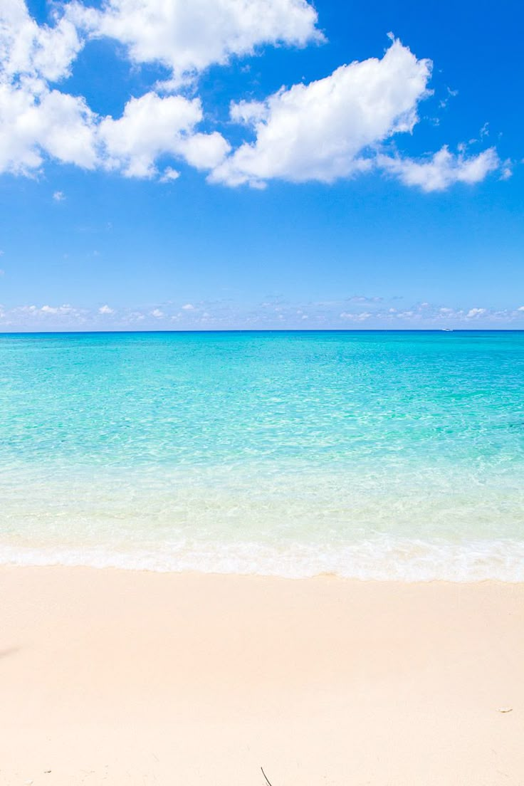 an empty beach with blue water and white clouds