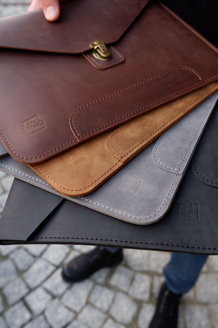 a person holding four different colored leather wallets