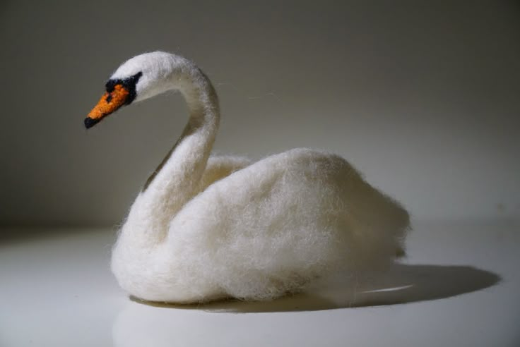 a white swan with an orange beak sitting on top of a pile of fluffy wool