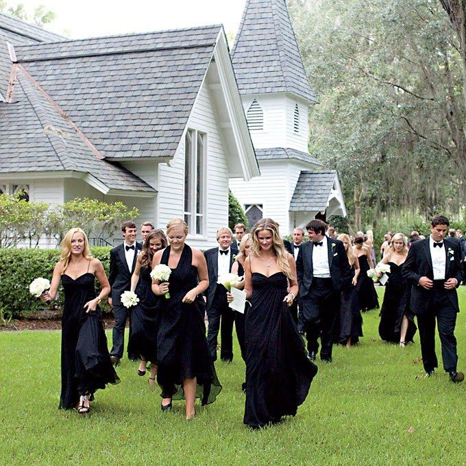 a large group of people in formal wear walking through the grass near a white house