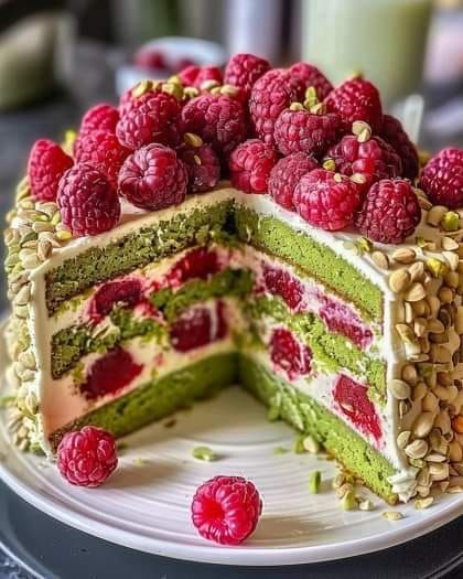 a layered cake with raspberries and pistachios on the top is ready to be eaten