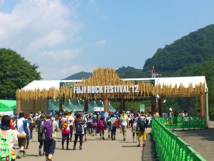 a group of people walking down a street next to a tall green gate with a sign that reads fuji rock festival 2012