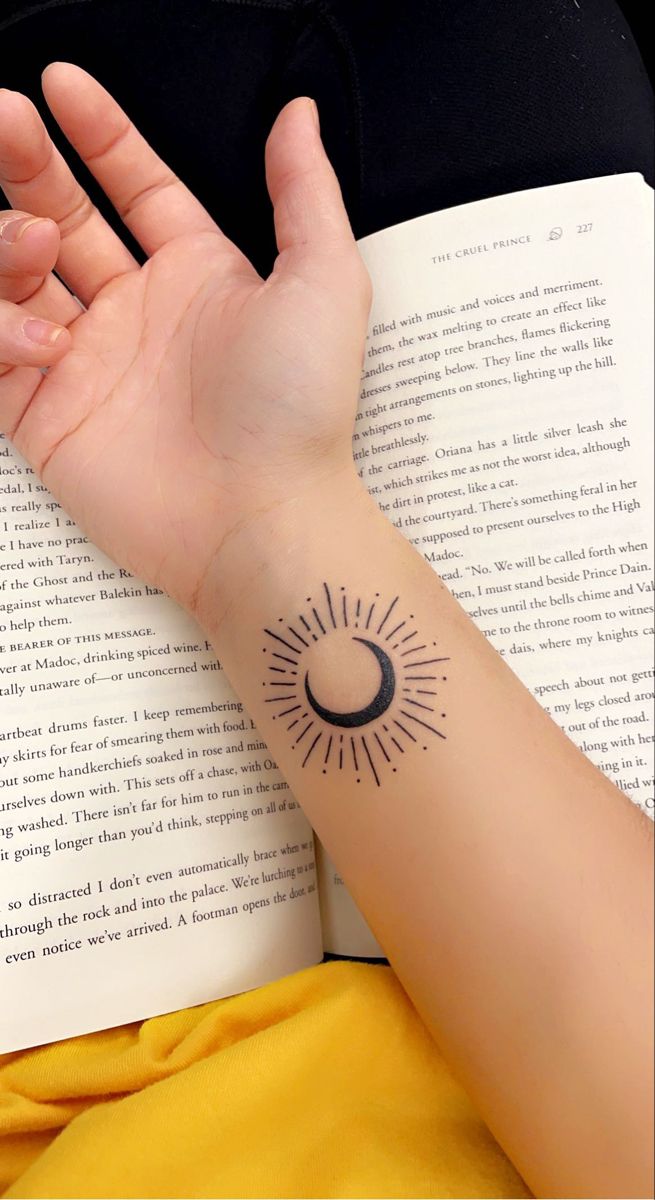 a woman's arm with a small sun and moon tattoo on it, sitting next to an open book