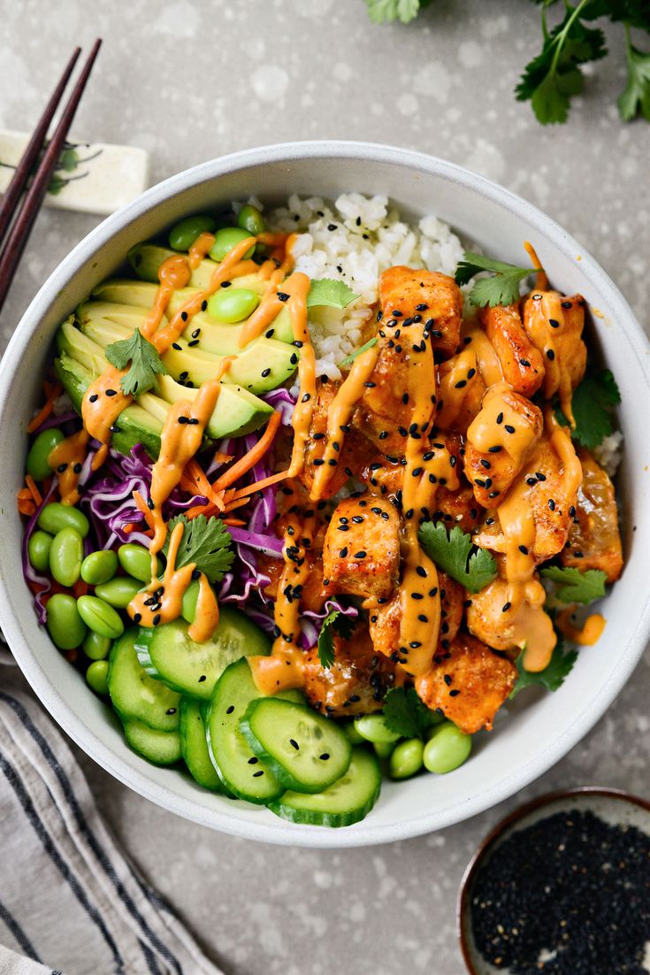 a white bowl filled with chicken and vegetables next to chopsticks on the side