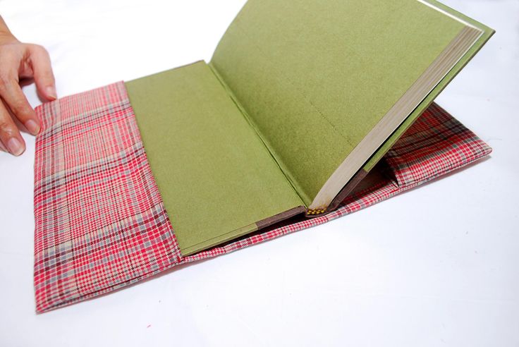 an open green book on top of a red and white checkered cloth with a person's hand reaching for it