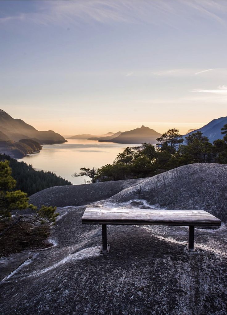 a wooden bench sitting on top of a rocky hill next to a lake and mountains