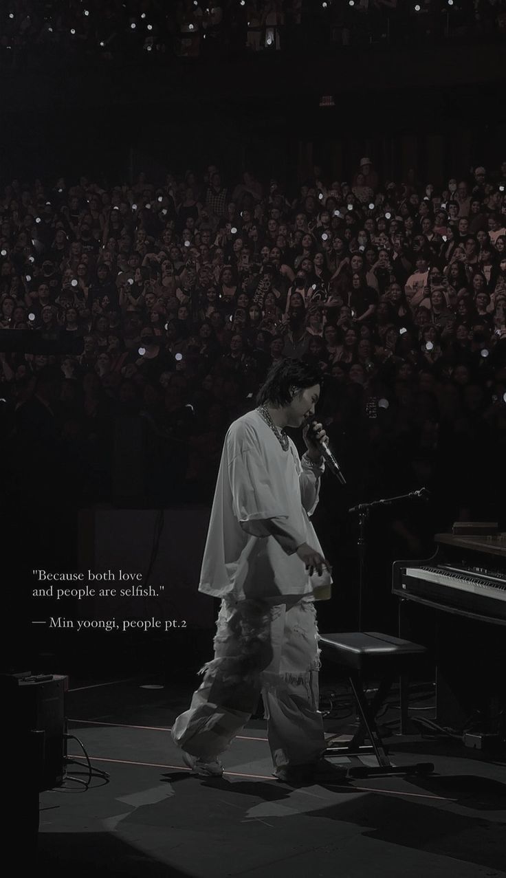 a man standing in front of a microphone on top of a stage next to a piano