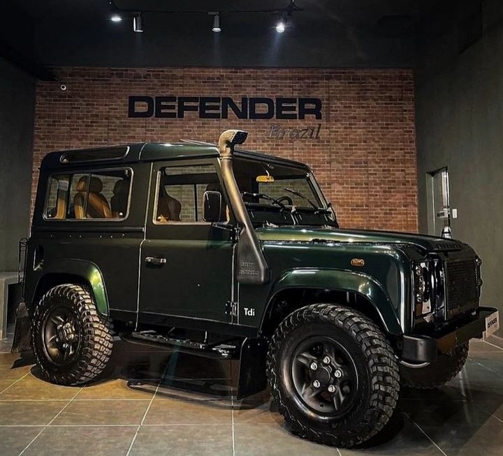 a green jeep is parked in front of a wall with the word defender on it