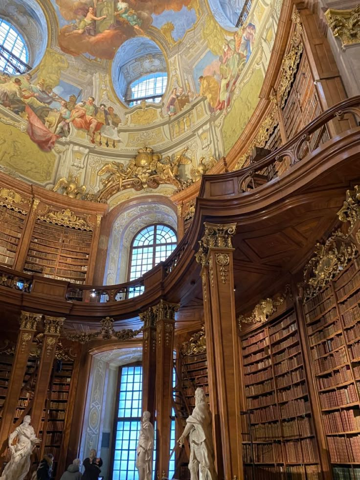 the interior of a library with statues and paintings on the ceiling, along with many bookshelves