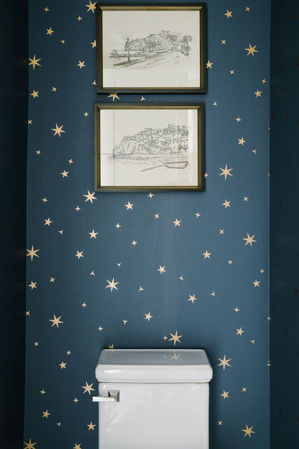 two framed pictures hang above a toilet in a blue bathroom with gold stars on the wall