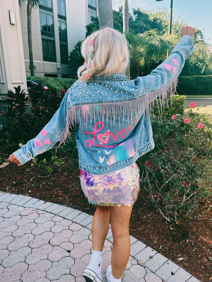 a woman with blonde hair wearing a jean jacket and colorful skirt walking down a sidewalk