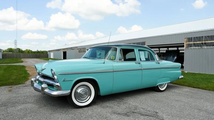 an old blue car parked in front of a building next to a grass covered field