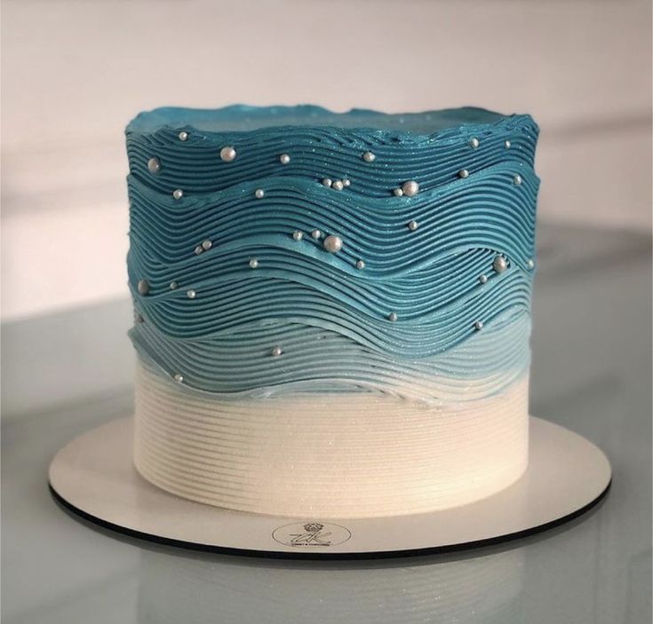 a blue and white cake sitting on top of a table next to a plate with silver beads