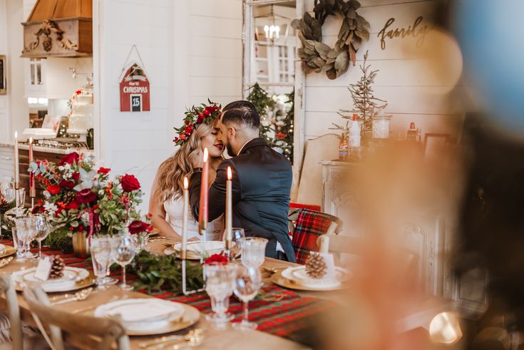 a man and woman sitting at a table with candles in front of them, surrounded by christmas decorations