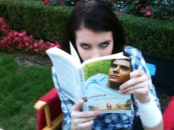 a woman sitting in a chair holding up a book to her face and looking at the camera