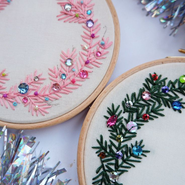 two embroidery hoops decorated with pink and green leaves, surrounded by tinsel crystals