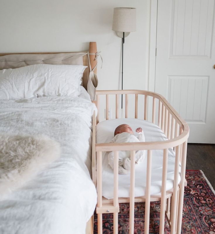 a baby sleeping in a crib next to a bed with white sheets and pillows